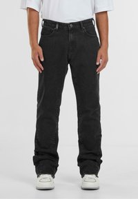 Zwarte denim jeans met een rechte pasvorm, vijf zakken, lichte vervaging en rafelige zoom, gecombineerd met witte sneakers.