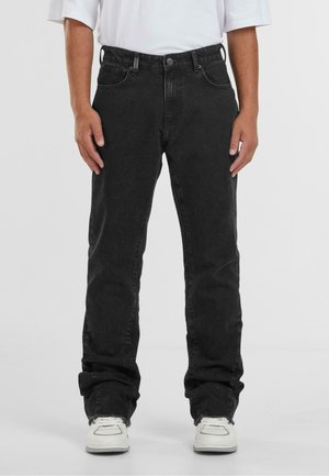 Black denim jeans with a straight fit, five-pocket design, slight fading, and frayed hems, paired with white sneakers.