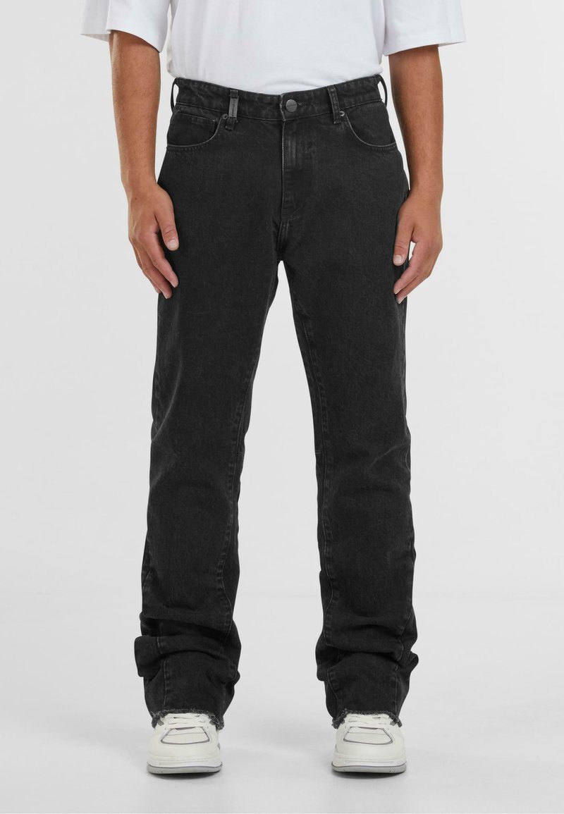 Zwarte denim jeans met een rechte pasvorm, vijf zakken, lichte vervaging en rafelige zoom, gecombineerd met witte sneakers.