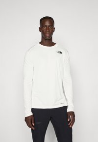 Long-sleeve white shirt made of lightweight fabric, featuring a small black logo on the upper left chest and a round neckline.