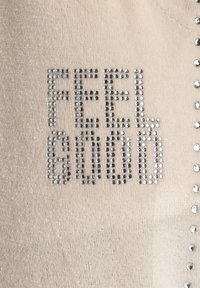 Beige stof met een zachte textuur, voorzien van de zin "FEEL GOOD" in zilveren strassstenen, benadrukt door kleine strassstenen langs één rand.