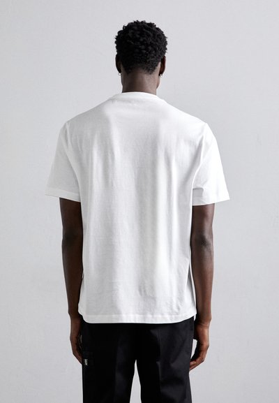 Camiseta de algodón blanca con mangas cortas y cuello redondo, con un ajuste holgado y una textura suave. La vista posterior no muestra logotipos visibles.