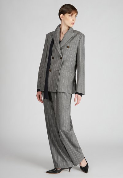 Blazer a doppio petto grigio a righe sottili con bottoni marroni, abbinato a pantaloni ampi coordinati e décolleté nero a punta.