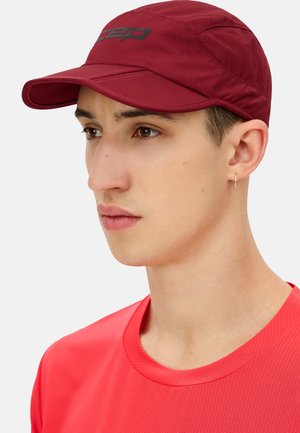 Maronenfarbige Laufmütze mit strukturiertem Schirm, geprägtem Logo auf der Vorderseite und atmungsaktivem Stoff. Der Hintergrund ist weiß, was die Mütze hervorhebt.