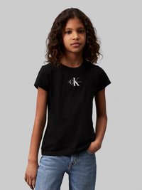 Camiseta de algodón negra de manga corta con un logotipo blanco de Calvin Klein. El diseño es casual y ajustado, combinado con jeans de azul claro.