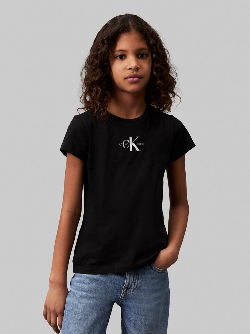 Camiseta de algodón negra de manga corta con un logotipo blanco de Calvin Klein. El diseño es casual y ajustado, combinado con jeans de azul claro.
