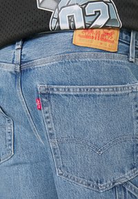 Jeans de mezclilla de color azul claro con corte recto, que presentan una etiqueta roja de Levi's y un característico diseño de costura en el bolsillo trasero. La textura es suave y ligeramente desgastada.