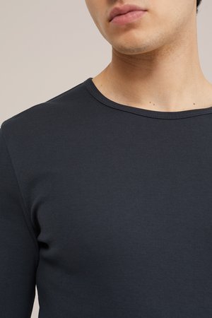 Close-up van de hals en bovenborst van een persoon die een donkergrijs, geribd, shirt met lange mouwen en een ronde hals draagt.
