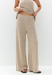 Pantalon large en tricot beige avec une finition texturée, doté d'une taille haute. Assorti à un haut sans manches, l'ensemble présente un look décontracté.