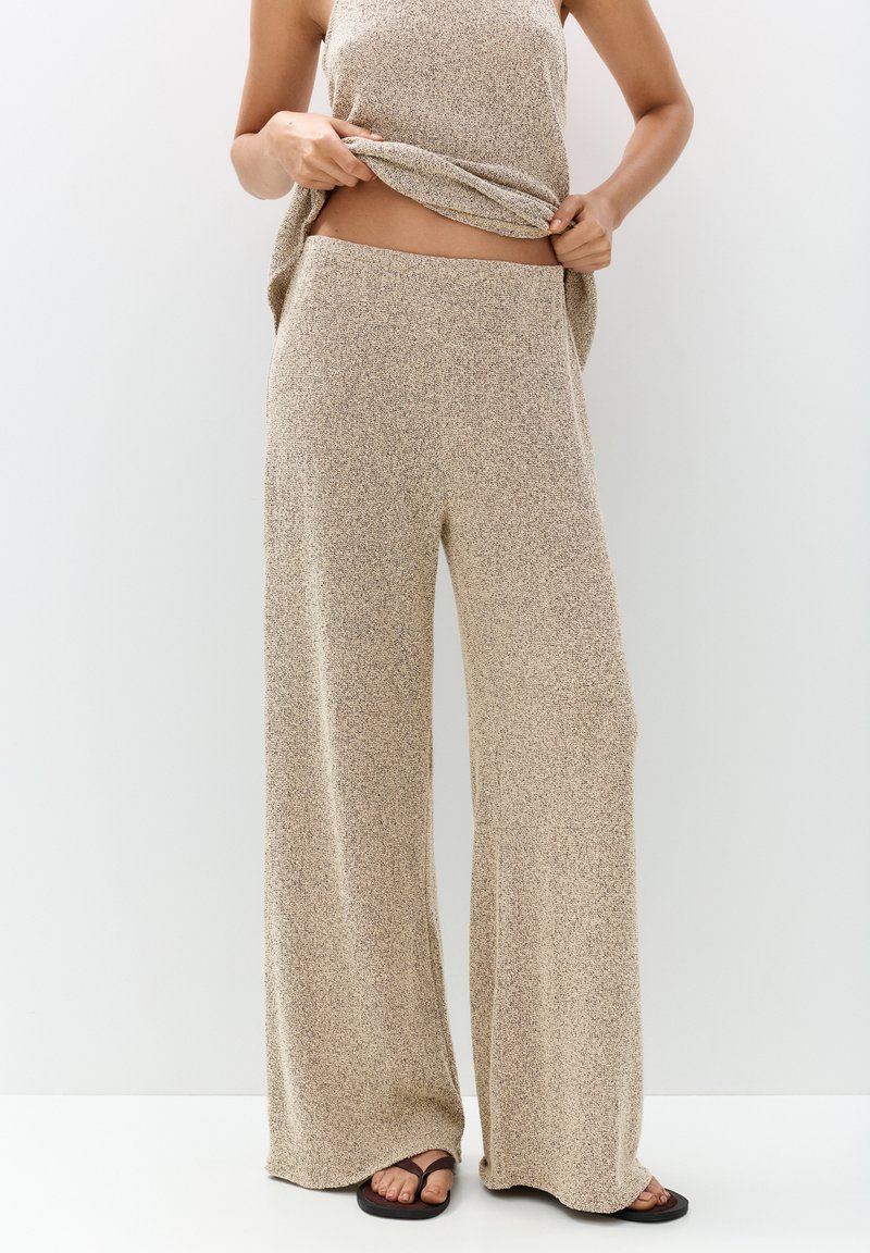 Pantalon large en tricot beige avec une finition texturée, doté d'une taille haute. Assorti à un haut sans manches, l'ensemble présente un look décontracté.