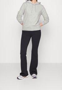 Grijze hoodie met trekkoorden, gedragen met zwarte flared broek en metalen sneakers. Glad textuur en casual pasvorm doorheen.