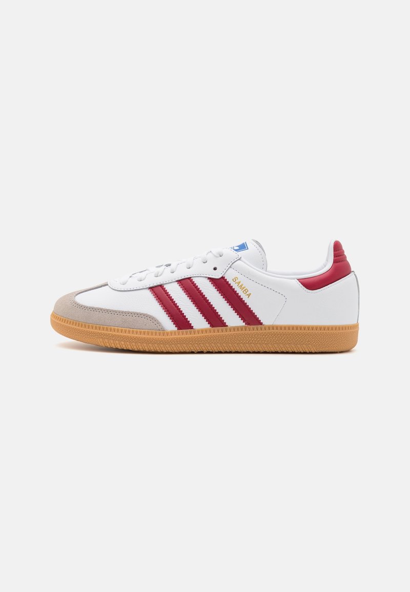 White sneaker with red stripes, gum sole, and light gray suede toe. Features blue tag, white laces, and branding on the side.
