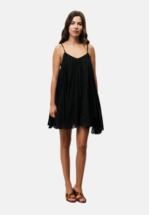 Schwarzes ärmelloses Kleid mit fließender Silhouette, gerafft an der Brust und weicher Textur. Getragen mit braunen Sandalen mit Riemen.