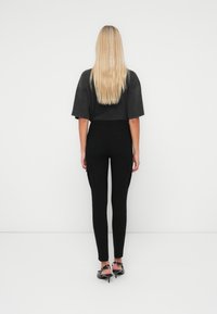 Zwarte cargobroek met zijzakken, strak ontwerp, gecombineerd met een losse, donkergrijze korte mouw top. Lang, steil blond haar zichtbaar.
