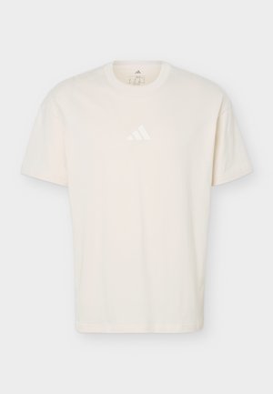 Kreemikas-valge lühikeste varrukatega T-särk ümarate kaelustega, millel on rinnal peen Adidas logo, esitletud lihtsalt helel taustal.