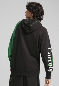 Felpa nera con accenti verdi, con un grande logo "Carrots" bianco sulla manica e una tasca a marsupio. Materiale morbido in misto cotone.