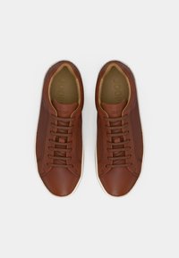 Braune Ledersneaker mit glatter Oberfläche, runder Zehenpartie und Schnürdesign. Die hellfarbene Sohle kontrastiert zum Obermaterial. Logo auf der Zunge.