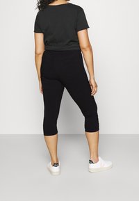 Mustat capri-trikoot, joissa on tiukka muotoilu ja joustava kangas, yhdistettynä mustaan lyhythihaiseen toppiin ja valkoisiin tennareihin, joissa on mustia yksityiskohtia.