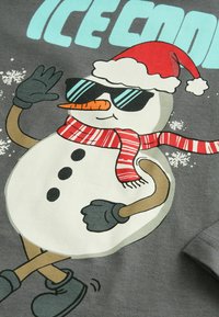 Tricou gri cu un om de zăpadă desenat în pălărie roșie de Moș Crăciun, ochelari de soare negri și o eșarfă cu dungi roșii, având butoane și mănuși negre.