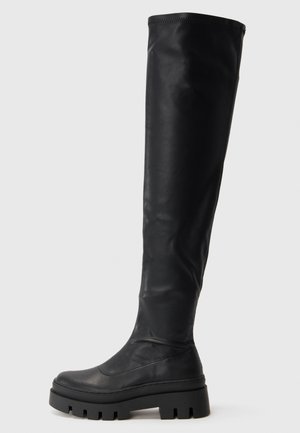 Black knee-high boot with chunky lug sole and smooth finish, featuring a rounded toe and slightly slouchy upper shaft.