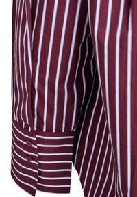 Bordo krekla piedurkne ar vertikālām baltām un gaiši zilām svītrām, ar aproci, kurā ir divi bordo pogas un horizontālas svītras.