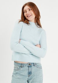 Lys blå, strikket sweater med høj hals og ribbede mansjetter. Har et cropped design, blød tekstur og afslappet pasform.