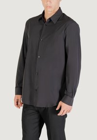 Camicia nera a maniche lunghe in tessuto morbido con colletto a punta, chiusura anteriore con bottoni e vestibilità morbida. Presenta polsini arrotolati.