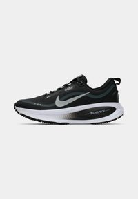Fekete Nike futócipő légáteresztő felsőrésszel, ezüst díszítésekkel és fehér ZoomX középtalppal. Jellemzője a texturált talp és a fekete fűző.