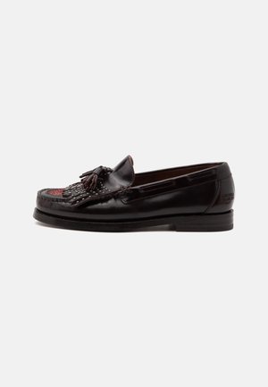 Mocasín de cuero negro con borlas, detalle de flecos y acentos de tachuelas, con tacón bajo y marca en relieve en el talón.