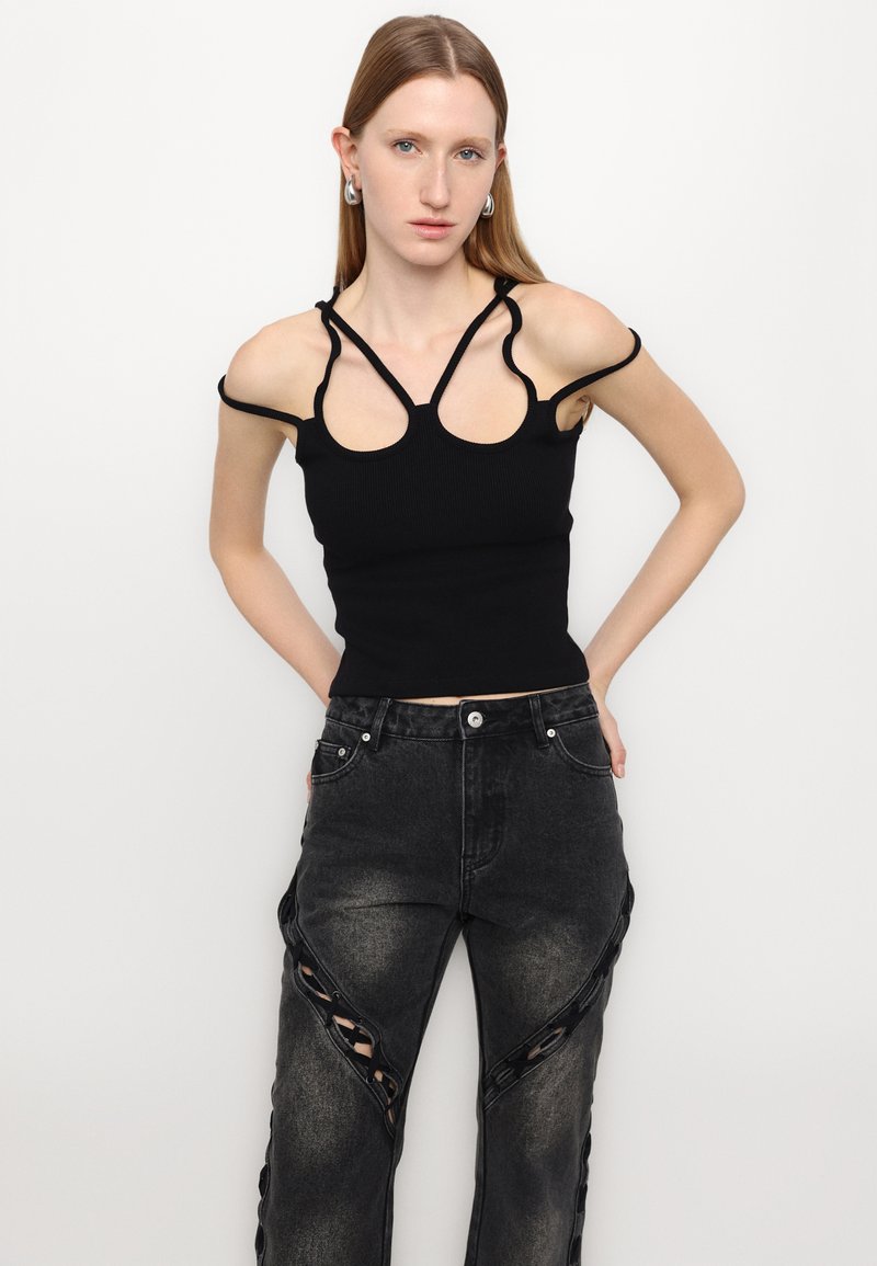 Top corto nero a coste con spalline sottili e spalle scoperte, abbinato a jeans neri strappati con dettagli a taglio lungo le gambe.