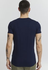 Navy blue lyhythihainen t-paita, jossa on mukautuva muotoilu, sileä pinta ja pyöreä kaula-aukko. Takakuvassa näkyy tatuointeja käsissä.