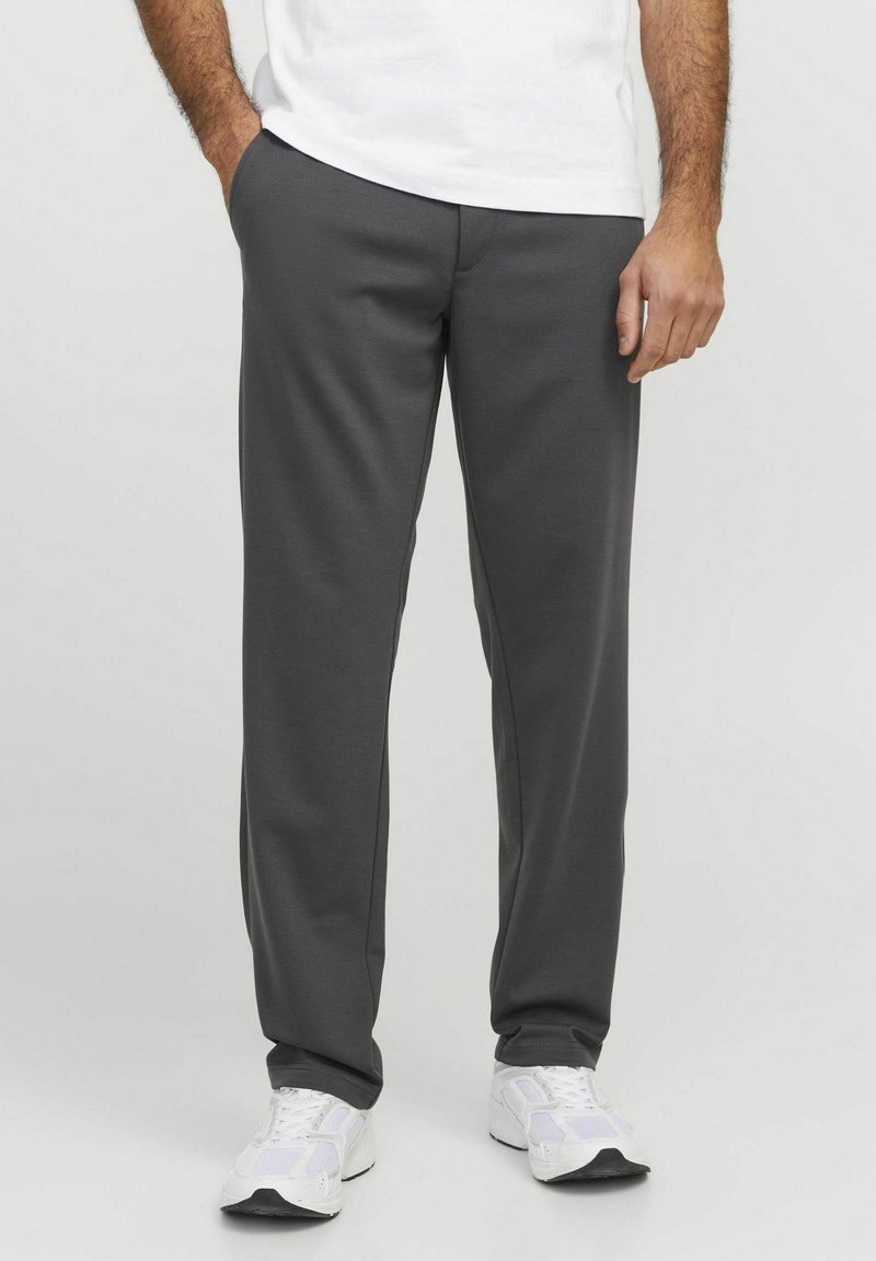 Pantalones deportivos grises en un tejido suave y elástico. Presentan un diseño de pierna recta con bolsillos y una cintura elástica. Combinados con zapatillas blancas.