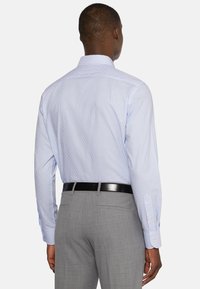 Jasnoniebieska koszula w paski z długimi rękawami, zapinanymi na guziki mankietami i plisą z tyłu. Szare, dopasowane spodnie z czarnym paskiem.