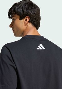 T-shirt en coton noir avec un col rond, des manches courtes, et un logo blanc à l'arrière, présentant une texture lisse.