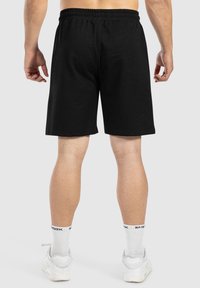 Pantalones cortos de algodón negros con cinturilla elástica, que llegan a la mitad del muslo. Tienen una textura suave y un diseño simple. Se llevan con calcetines y zapatos blancos.