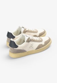 Baskets en cuir crème avec des accents en suède beige et gris. Présente un logo de crâne sur le côté et un capot de talon noir. Semelle en caoutchouc, design classique.