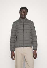 Grey puffer jacket with a stand collar, horizontal quilted design, front zipper closure, and side pockets. Smooth texture and sleek fit.