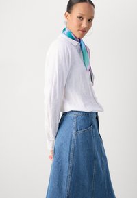 Witte linnen shirt, hoge taille spijkerrok in blauw, en een kleurrijke zijden sjaal met aqua- en paarstinten, met een gladde textuur.