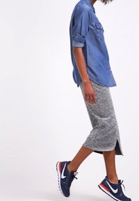 Camicetta in denim con bottoni, gonna midi grigia mélange con spacchi laterali e sneakers blu con dettagli rossi. Outfit casual a strati.