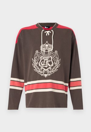 Brown long-sleeve shirt featuring a front graphic with a crown and skull, red shoulder accents, and horizontal stripes in cream and red.