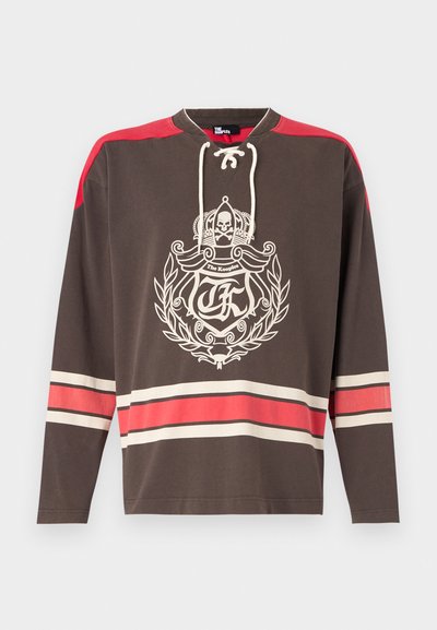 Camisa de manga larga marrón con un gráfico frontal que presenta una corona y una calavera, acentos rojos en los hombros y rayas horizontales en crema y rojo.