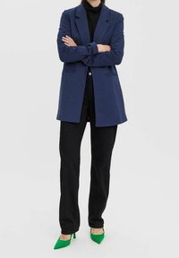 Marinblazer med slag, framfickor och en skräddarsydd passform, kombinerad med svarta byxor och gröna spetsiga klackar.