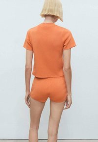 Kort orange stickad topp med korta ärmar och matchande shorts, båda med en mjuk textur och minimalistisk design. Bakifrån visas.