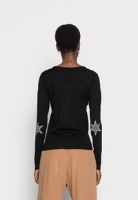 Svart tröja med långa ärmar och silverfärgade stjärnapplikationer på armbågarna. Mjuk stickad material med en figurnära design och ribbat nederkant.