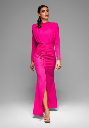 Fuchsia långärmad klänning med rynkdetaljer i midjan och en snitt framtill, gjord av ett mjukt tyg. Modellen bär guldfärgade klackar med remmar.