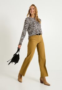 Blusa de manga larga blanca con estampado de leopardo negro y marrón, combinada con pantalones de pierna ancha de talle alto en mostaza y botines marrón claro.