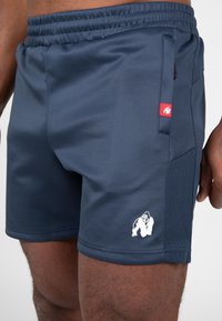 Marineblauwe sportshorts gemaakt van gladde stof, met een rood logo-patch en mesh zijpanelen voor ademend vermogen. Witte gorilla grafische details.