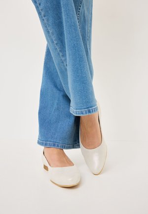 Scarpe bianche flat realizzate in materiale morbido, con punta rotonda e tacco basso, abbinate a jeans a gamba larga blu chiaro.