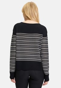 Gestreifter schwarz-weißer Pullover mit lockerem Schnitt, geripptem Saum und offenen Strickdetails an den Ärmlen. Die Rückansicht zeigt ein horizontales Streifenmuster.