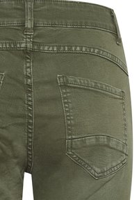 Jeans de mezclilla verde oliva con una textura suave, diseño de cinco bolsillos y costuras reforzadas. Los bolsillos traseros son rectangulares con costuras sutiles.